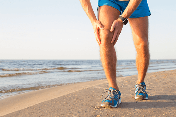 runner struggling with knee pain on beach